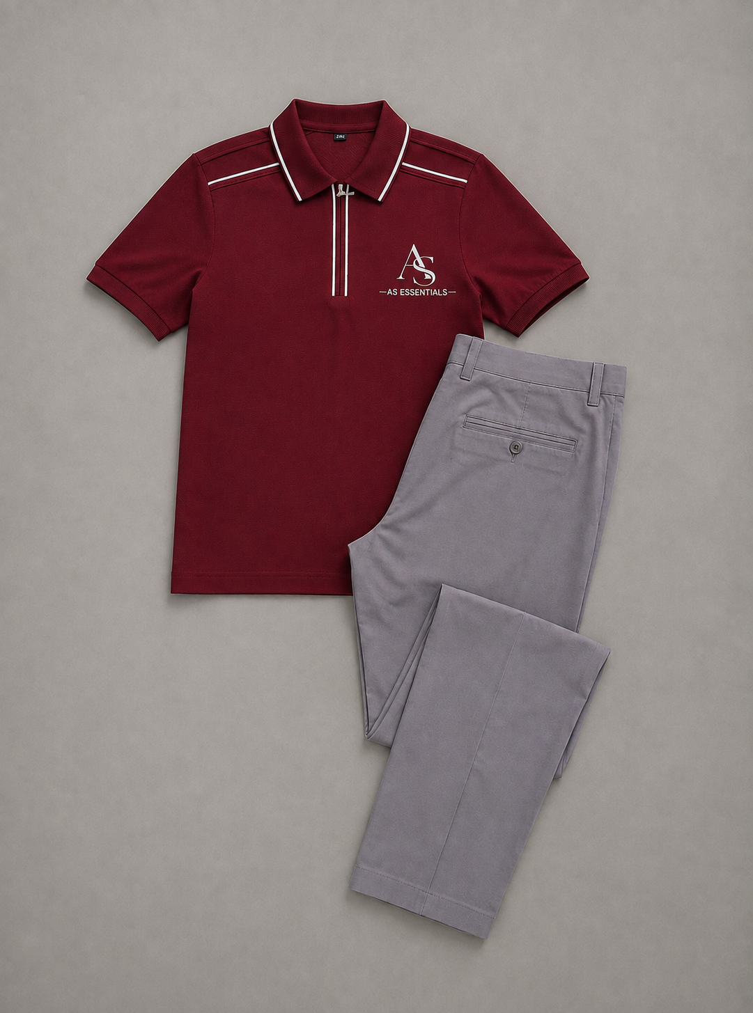 Polo rouge bordeaux AS ESSENTIALS à col zippé et liserés blancs, présenté à plat avec un pantalon gris.