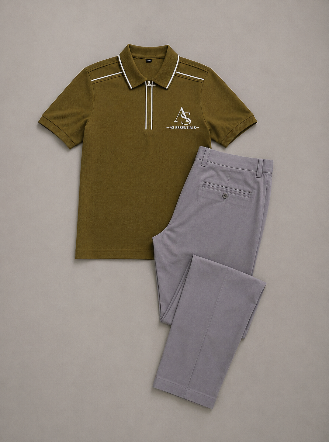 Polo vert olive AS ESSENTIALS à col zippé et liserés blancs, présenté à plat avec un pantalon gris.
